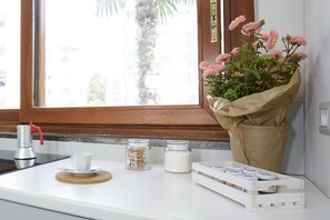 Una encimera de cocina con una cafetera, una taza, dos tarros y un ramo de flores.