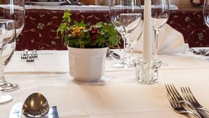 A dining table set with white tablecloth, silverware, wine glasses, a candle, and a potted plant. - Jägerhof Geniesser & Wanderhotel (San Leonardo in Passiria)