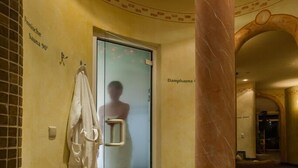A hallway with a glass door leading to a sauna, a marble column, and a tiled floor. - Jägerhof Geniesser & Wanderhotel (San Leonardo in Passiria)