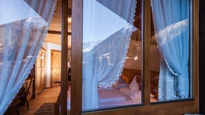 A cozy room with a bed, wooden walls, and a window with lace curtains. - Jägerhof Geniesser & Wanderhotel (San Leonardo in Passiria)
