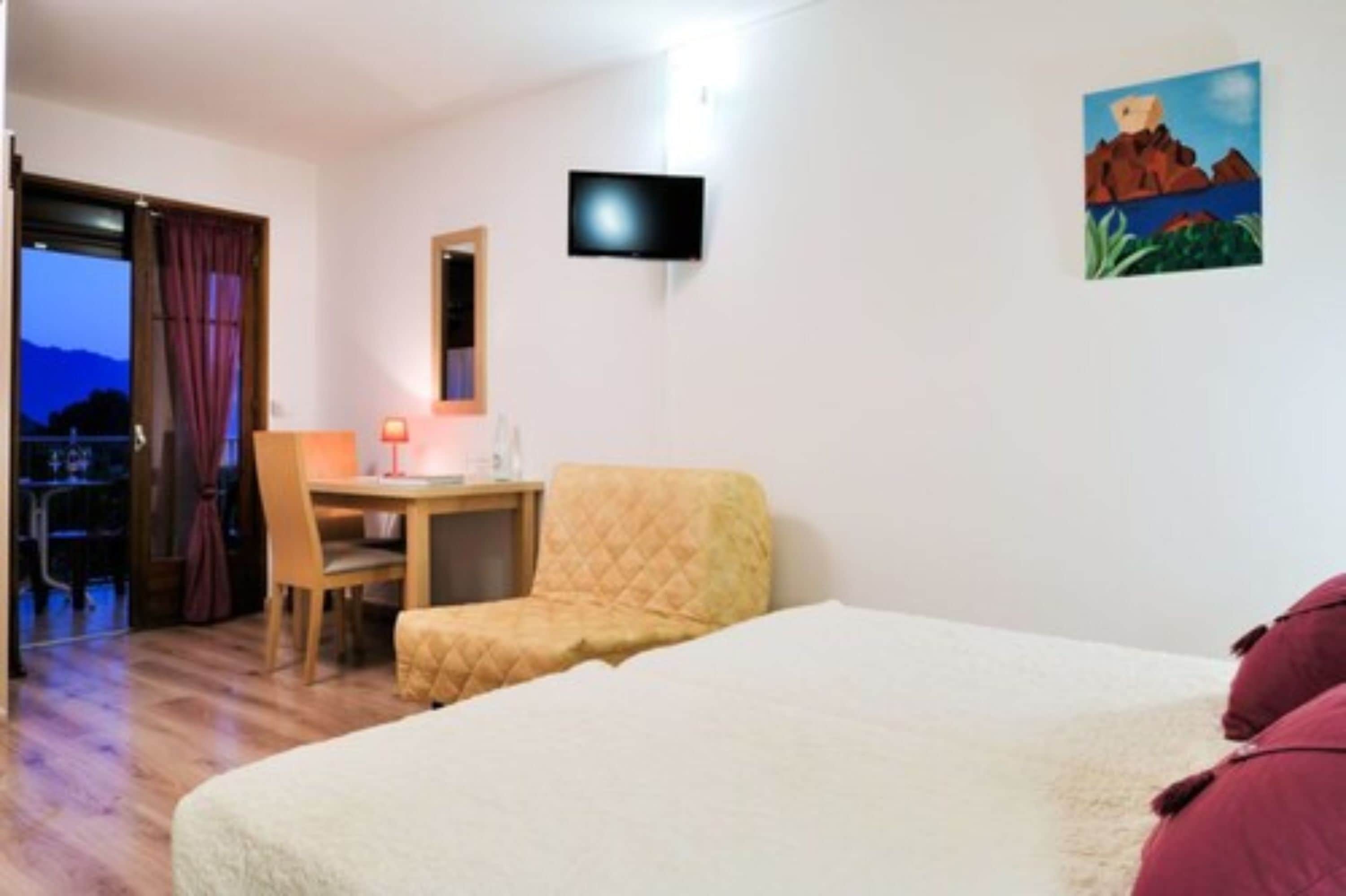 Una habitación de hotel con cama, escritorio, silla, televisión y un cuadro en la pared.
