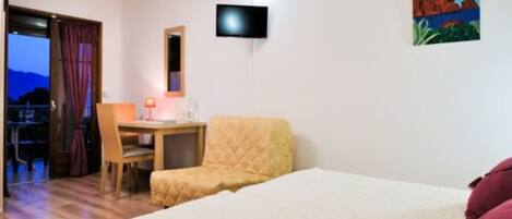Una habitación de hotel con cama, escritorio, silla, televisión y un cuadro en la pared.