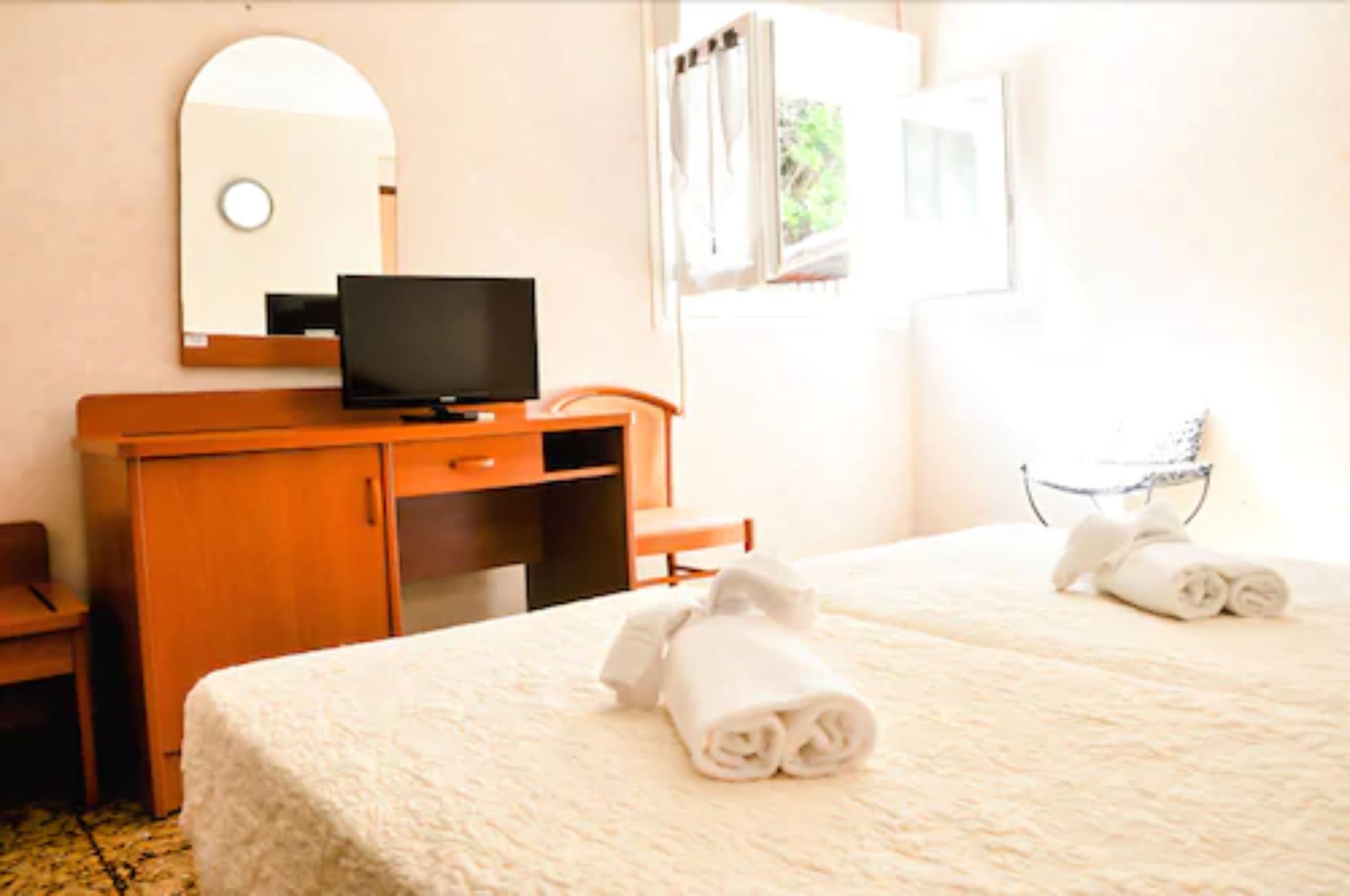 Habitación de hotel con cama, televisor sobre una cómoda de madera, espejo y ventana con cortinas.