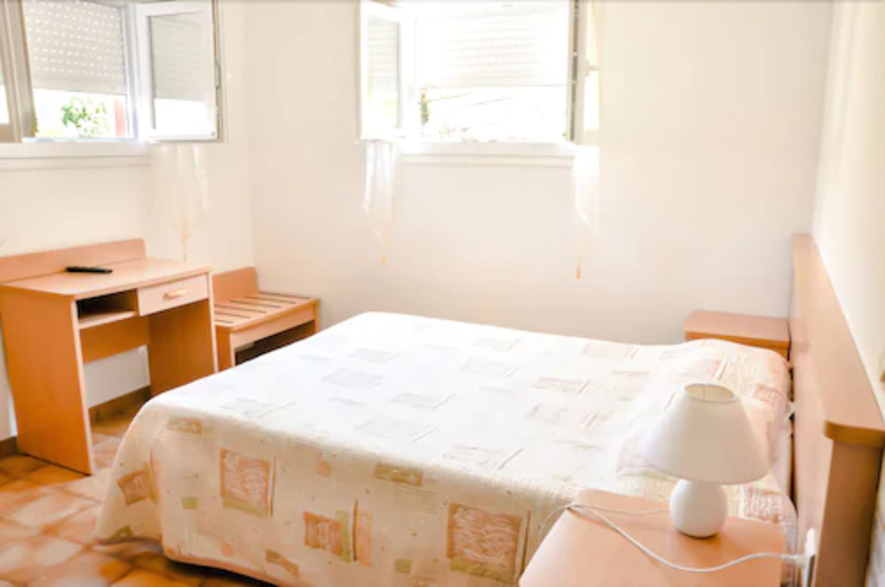 Quarto com cama, escrivaninha, cadeira, mesa de cabeceira e janela.