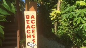 Een houten bord met een wijzende hand en de tekst 'ACCESS BEACH', dat een pad naar het strand aangeeft.