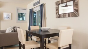 Een eetgedeelte met een donker houten tafel, zes stoelen, een witte kom, een plafondventilator en een raam met blauwe gordijnen.