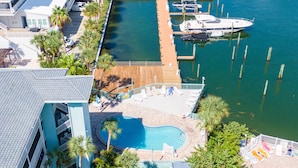 A marina with boats docked, a swimming pool, and a building with a balcony overlooking the water.