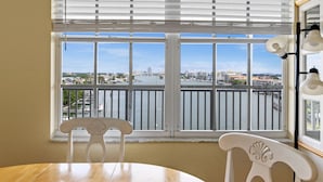 A room with a large window overlooking a cityscape and water. There is a wooden table and two white chairs.
