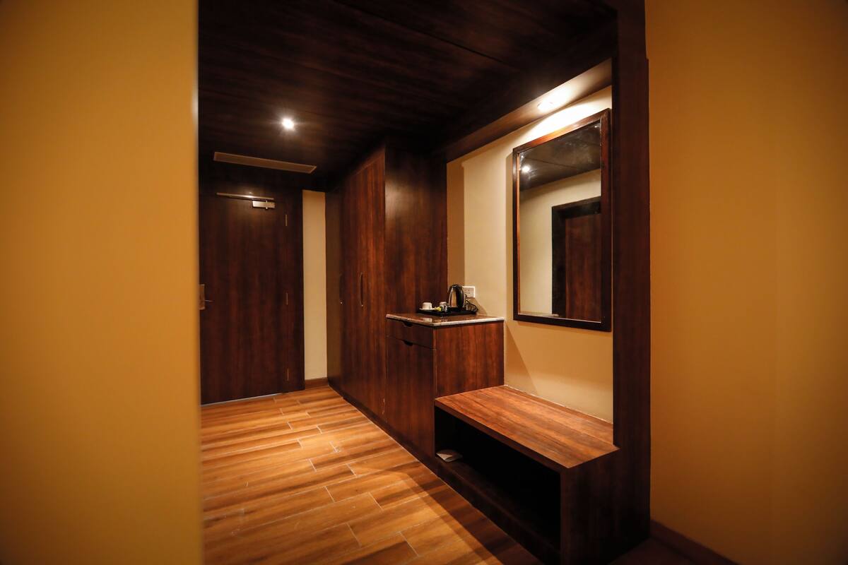 Un pasillo con suelo de madera, un banco, un espejo y una pequeña mesa con un hervidor.