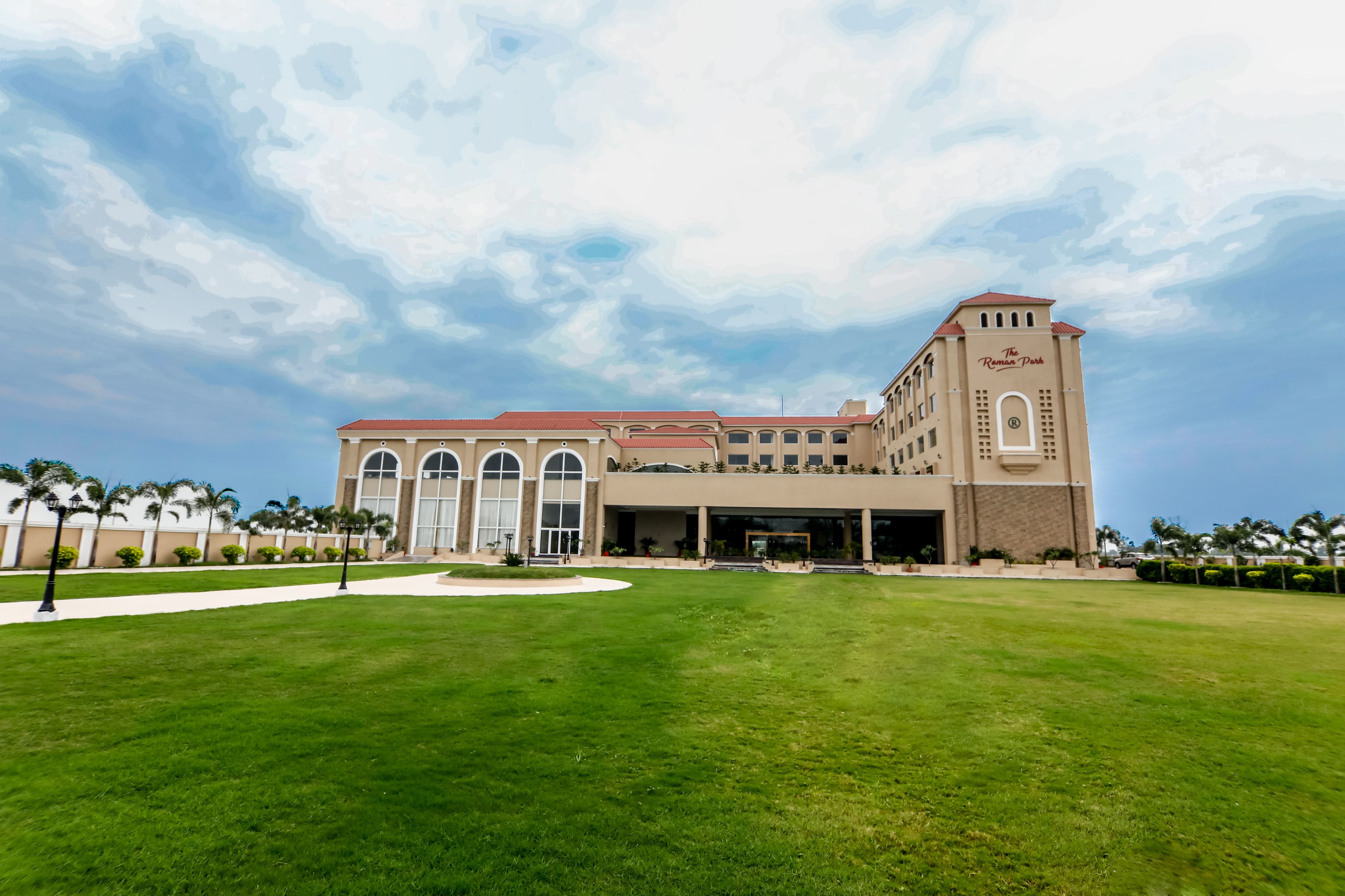 A large hotel with a central tower, multiple wings, and a well-maintained lawn.