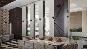Un comedor moderno con mobiliario estampado, ventanas amplias e iluminación decorativa en la pared.