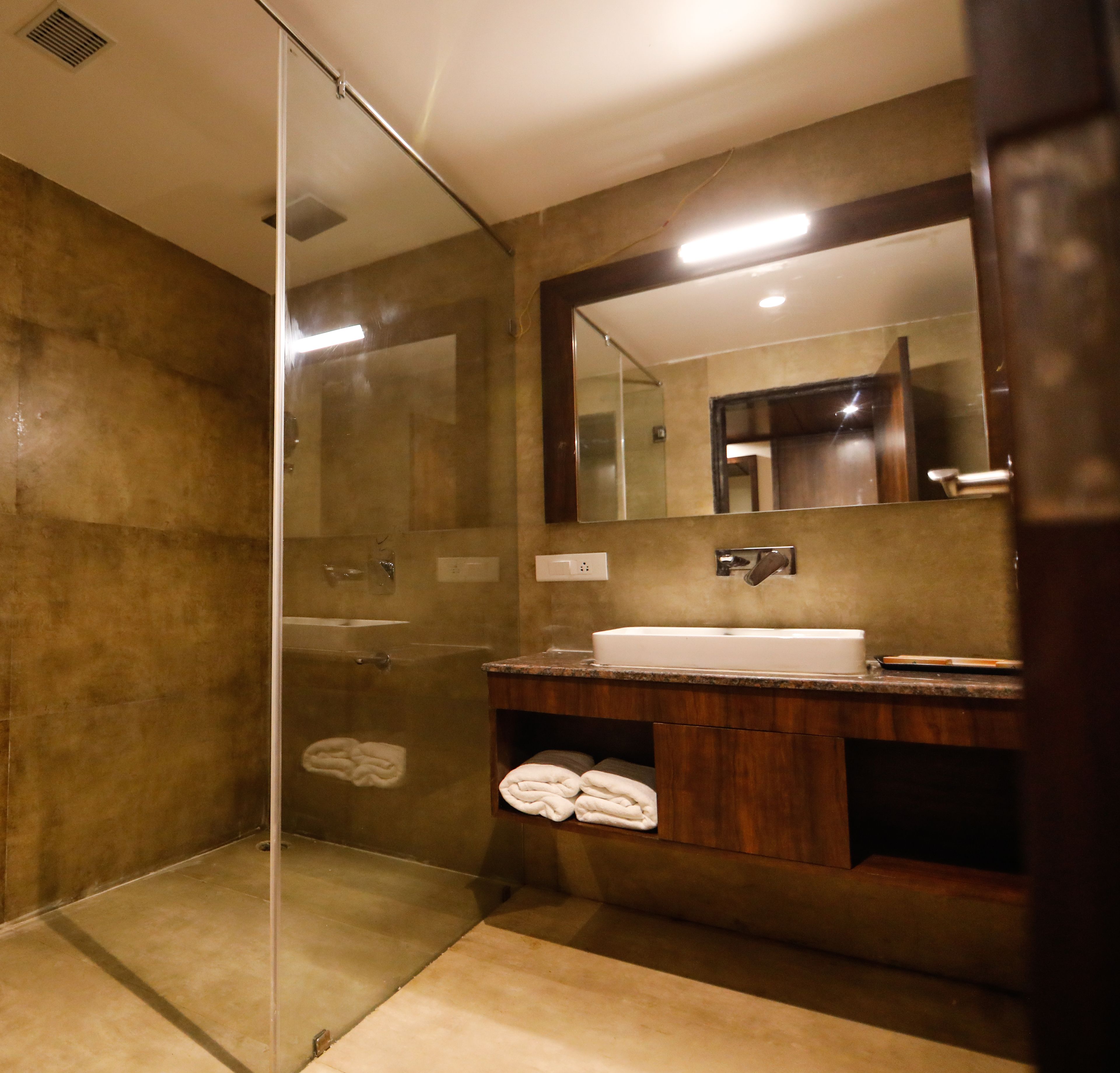 Un baño moderno con ducha acristalada, un espejo grande y un mueble de tocador de madera.