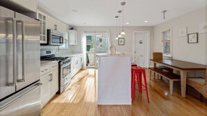 A modern kitchen with stainless steel appliances, wooden flooring, and a central island with stools. - SEA BRIGHT BEACH BEAUTY. 1 block to beach, restaurants, entertainment. 3br, Deck (Sea Bright)