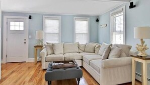 A living room with a sectional sofa, a small ottoman, and a lamp on a side table. - SEA BRIGHT BEACH BEAUTY. 1 block to beach, restaurants, entertainment. 3br, Deck (Sea Bright)