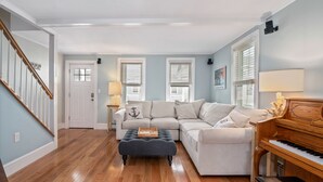 A living room with a sectional sofa, a wooden floor, a piano, and a staircase. - SEA BRIGHT BEACH BEAUTY. 1 block to beach, restaurants, entertainment. 3br, Deck (Sea Bright)