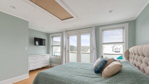 A bedroom with a large bed, a dresser, a television, and a balcony view. - SEA BRIGHT BEACH BEAUTY. 1 block to beach, restaurants, entertainment. 3br, Deck (Sea Bright)