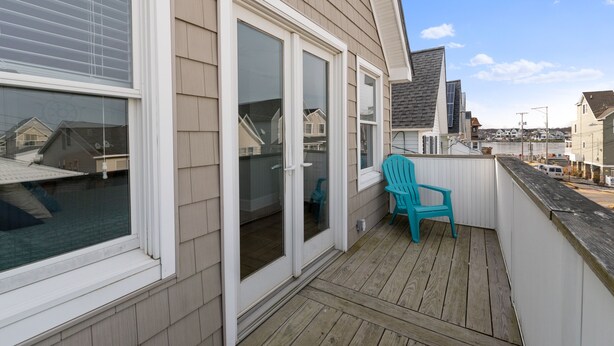 A balcony with a wooden deck, a turquoise chair, and a sliding glass door leading to a covered patio area. - SEA BRIGHT BEACH BEAUTY. 1 block to beach, restaurants, entertainment. 3br, Deck (Sea Bright)
