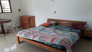 Una camera da letto con un letto di legno, un comodino in legno, una sedia, una cassettiera in legno e un tavolino rotondo.