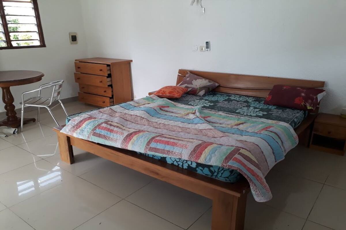 A bedroom with a wooden bed, a small wooden nightstand, a chair, a wooden dresser, and a round table.