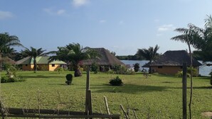 Una zona erbosa con case a tetto di paglia e uno specchio d'acqua sullo sfondo.
