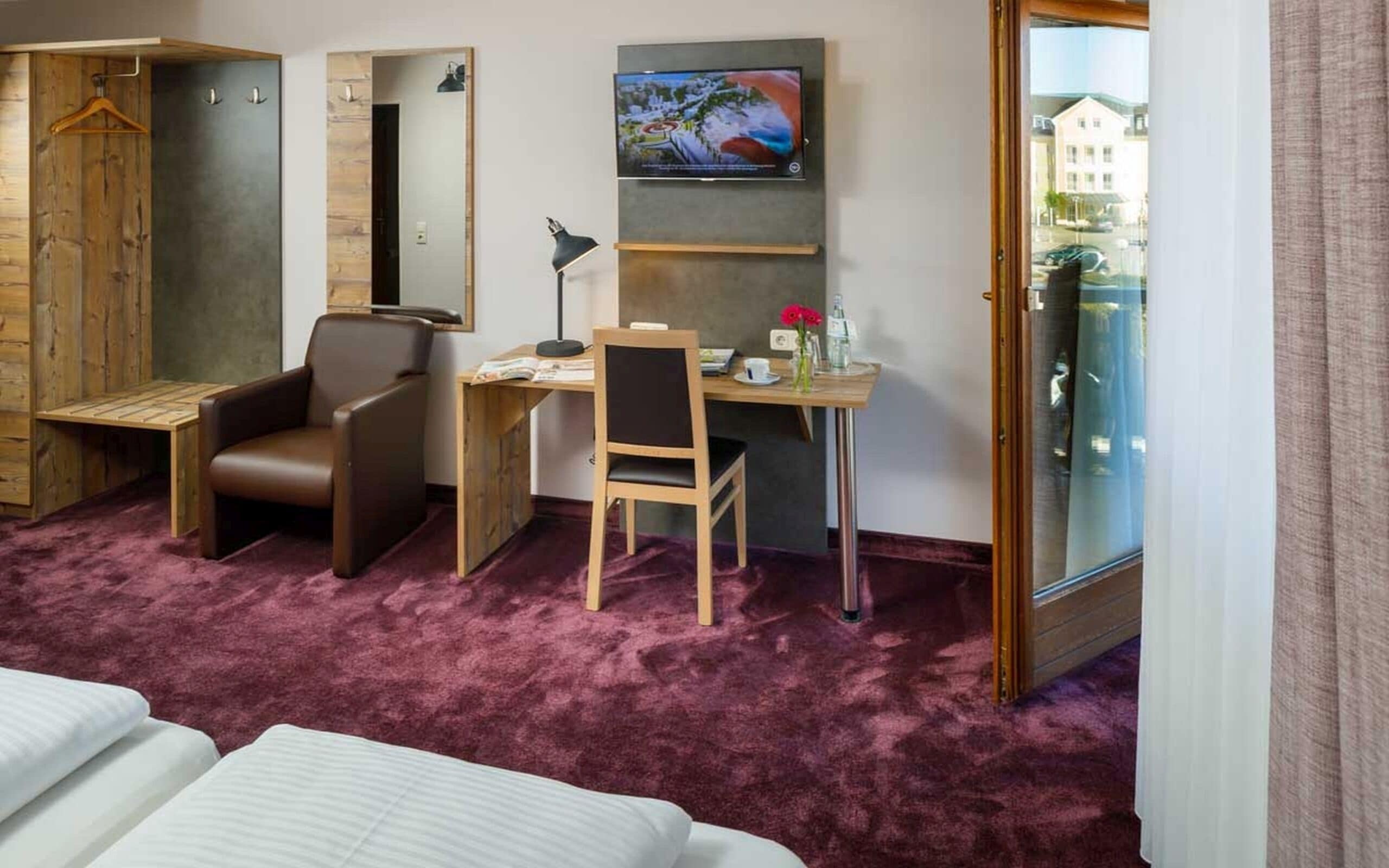 Habitación de hotel con cama, escritorio, silla, armario y televisor en la pared.