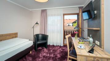 A hotel room with a bed, a desk with a chair, a TV, and a window with curtains.