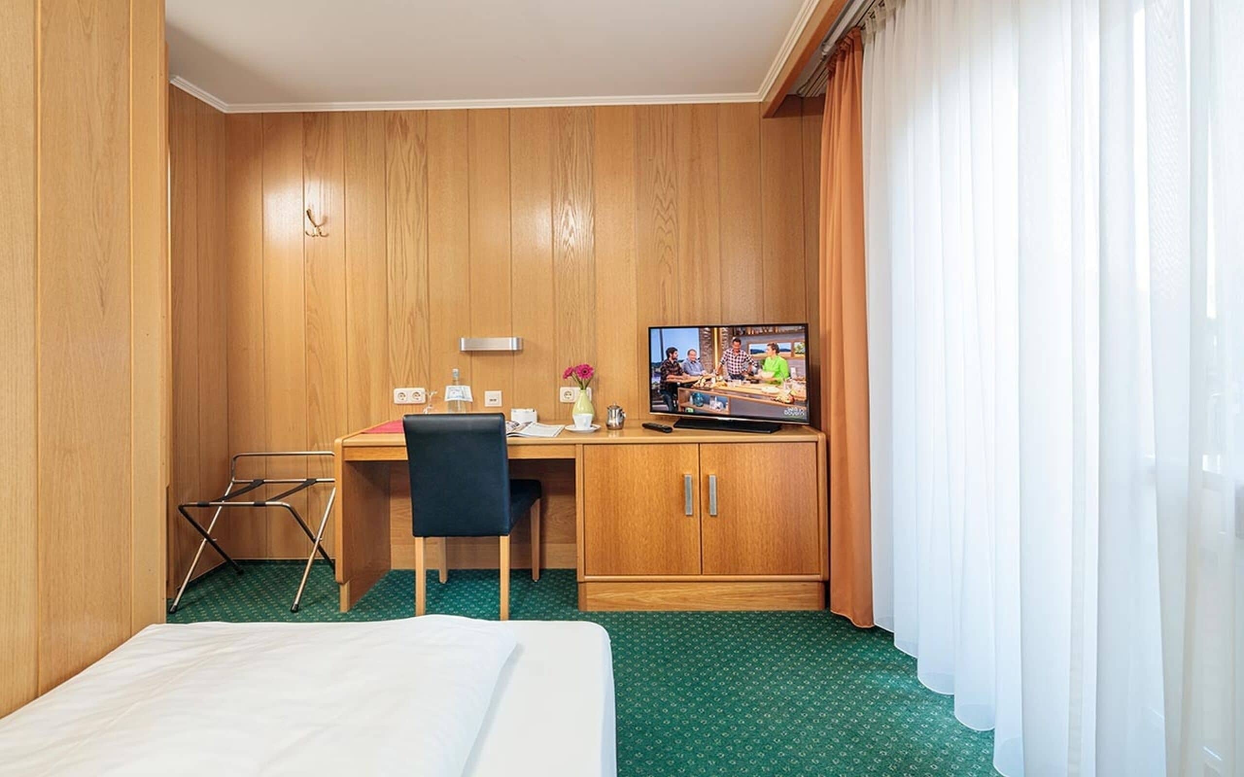 A hotel room with a bed, a desk with a chair, a television, and a wardrobe.