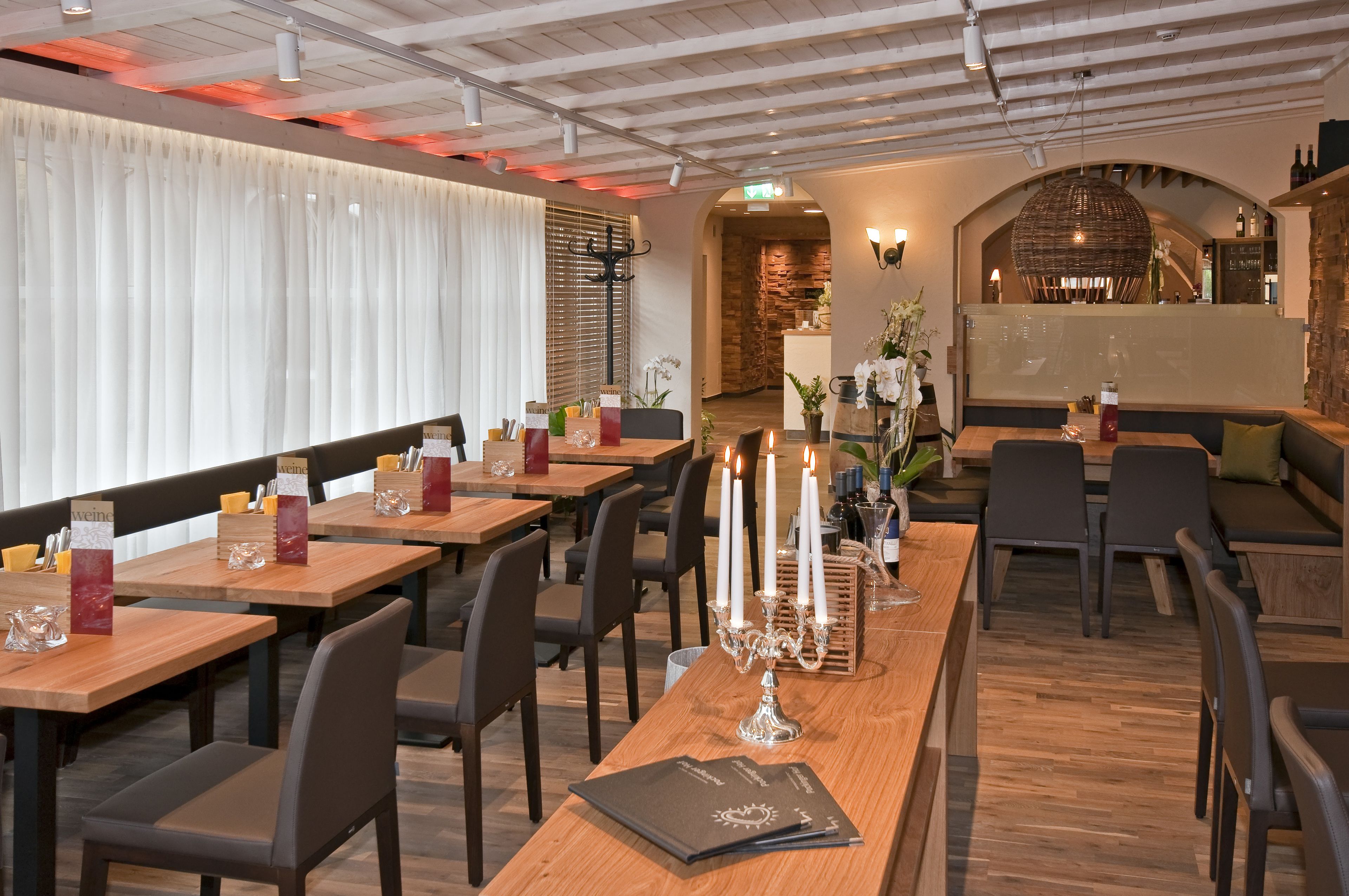 A restaurant with wooden tables, black chairs, and a long wooden counter.