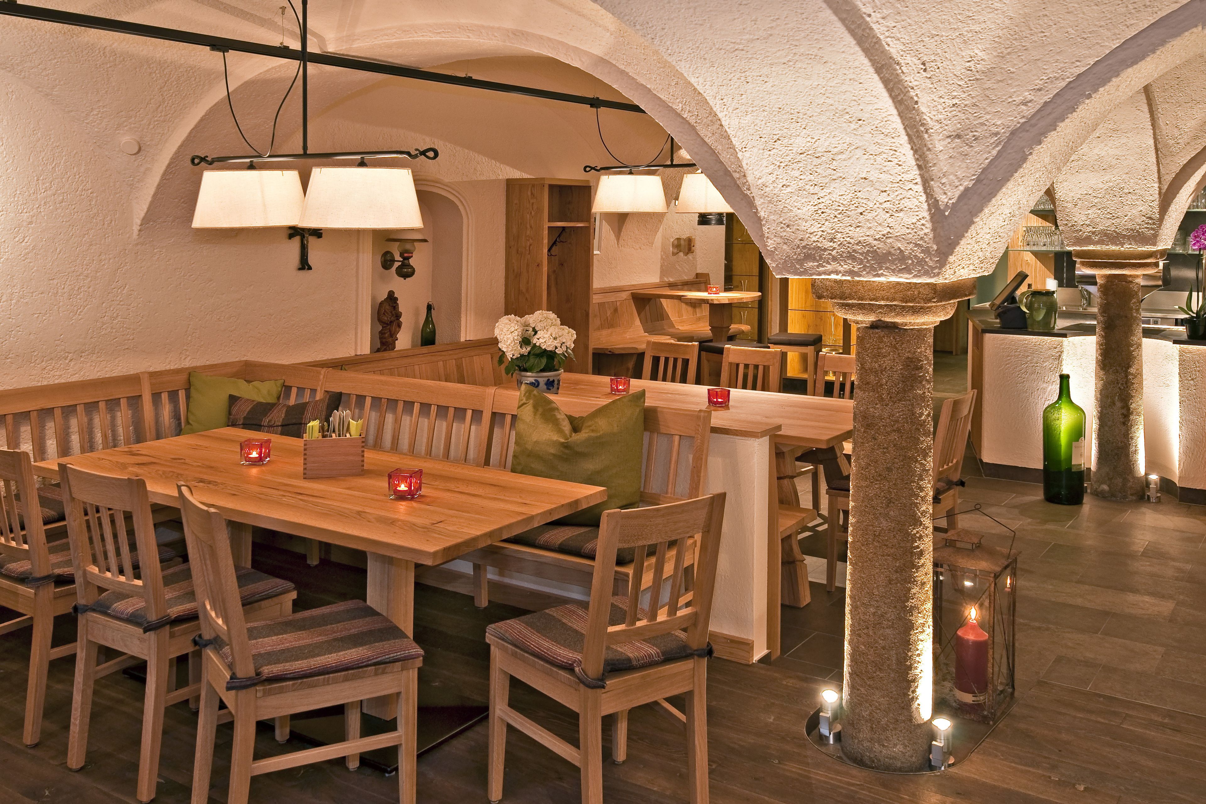 Un restaurante acogedor con mesas y bancos de madera, pilares de piedra e iluminación cálida.