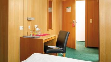 Habitación de hotel con cama, escritorio y silla, espejo, puerta y alfombra verde.