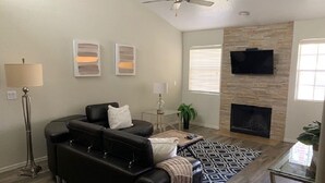 A living room with a black leather sofa, a coffee table, a patterned rug, a fireplace, and a flat-screen TV mounted on the wall. - With snowbirds landing here you will be at home. City of Scottsdale: 2027801. (Scottsdale)