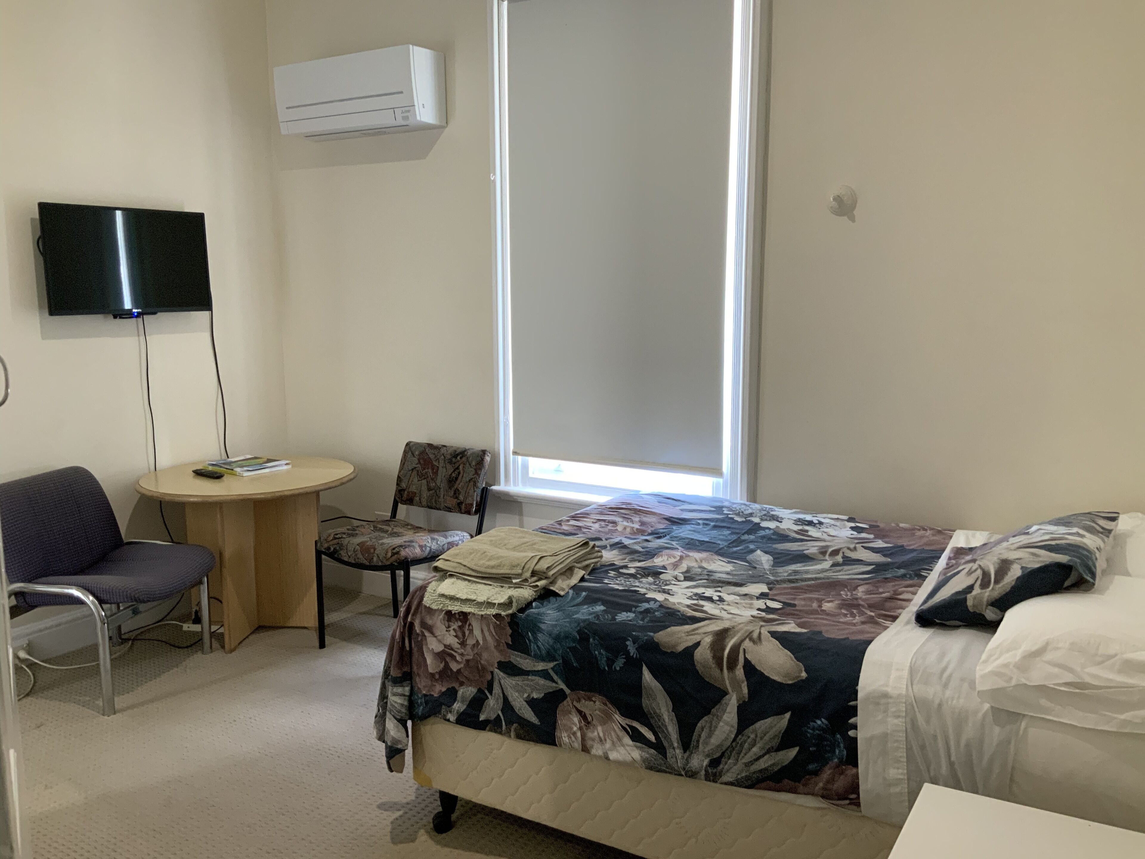 Une chambre d’hôtel équipée d’un lit, d’une chaise, d’une petite table, d’un téléviseur et d’un appareil de climatisation.