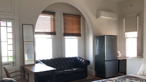 Ein Zimmer mit einer schwarzen Ledersofa, einem kleinen Tisch, einem Kühlschrank und einem Bett mit einem Blumenüberwurf.