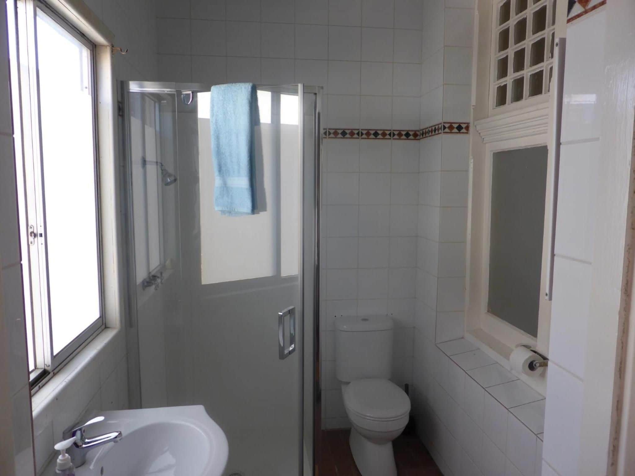 Een badkamer met een douchecabine van glas, een wit toilet en een wastafel met kraan.