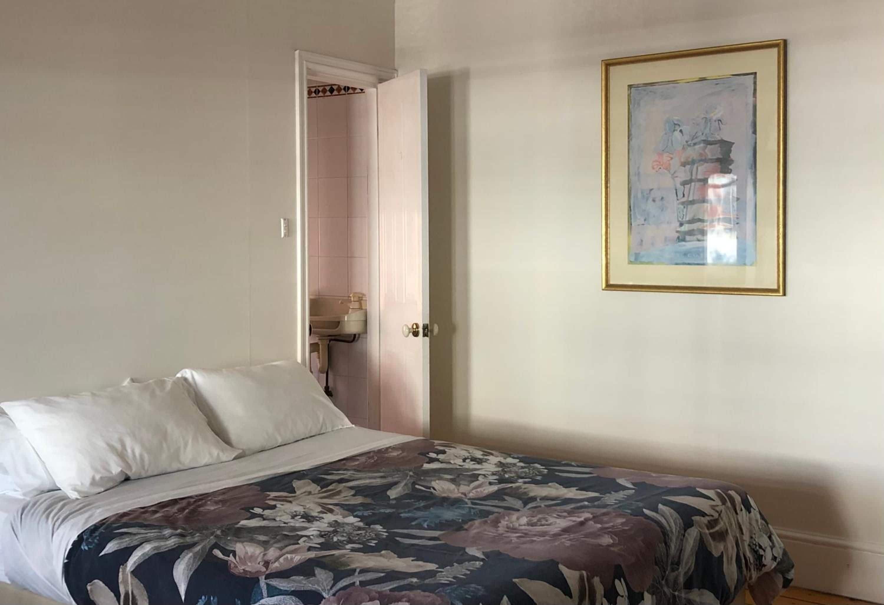 Un dormitori amb un llit, una porta que dona a un bany i un quadre encimbellat a la paret.