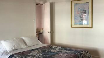 Une chambre à coucher avec un lit, une porte donnant sur une salle de bain et un tableau encadré accroché au mur.