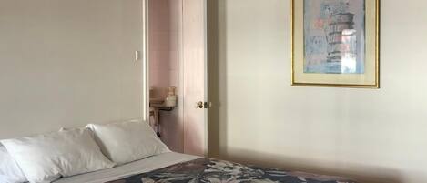 Un dormitori amb un llit, una porta que dona a un bany i un quadre encimbellat a la paret.