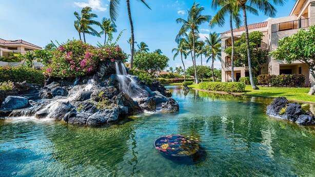 A resort pool with clear water, a waterfall, and palm trees. - 🏖️Ground Floor Condo | Lagoon Views + Large Lanai + A/C (Waikoloa)