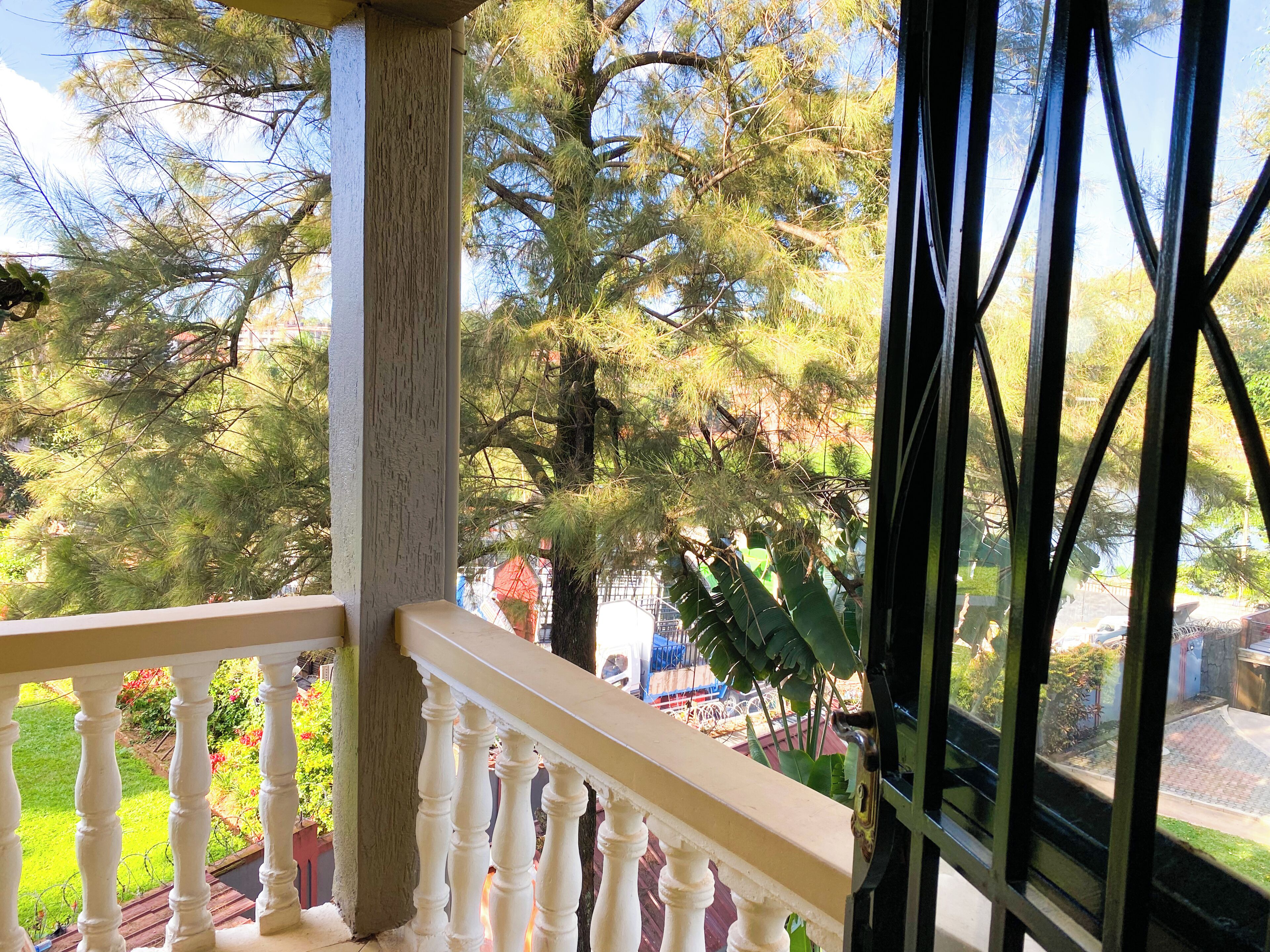 A balcony with a railing, a view of trees, and a glimpse of the surrounding area.