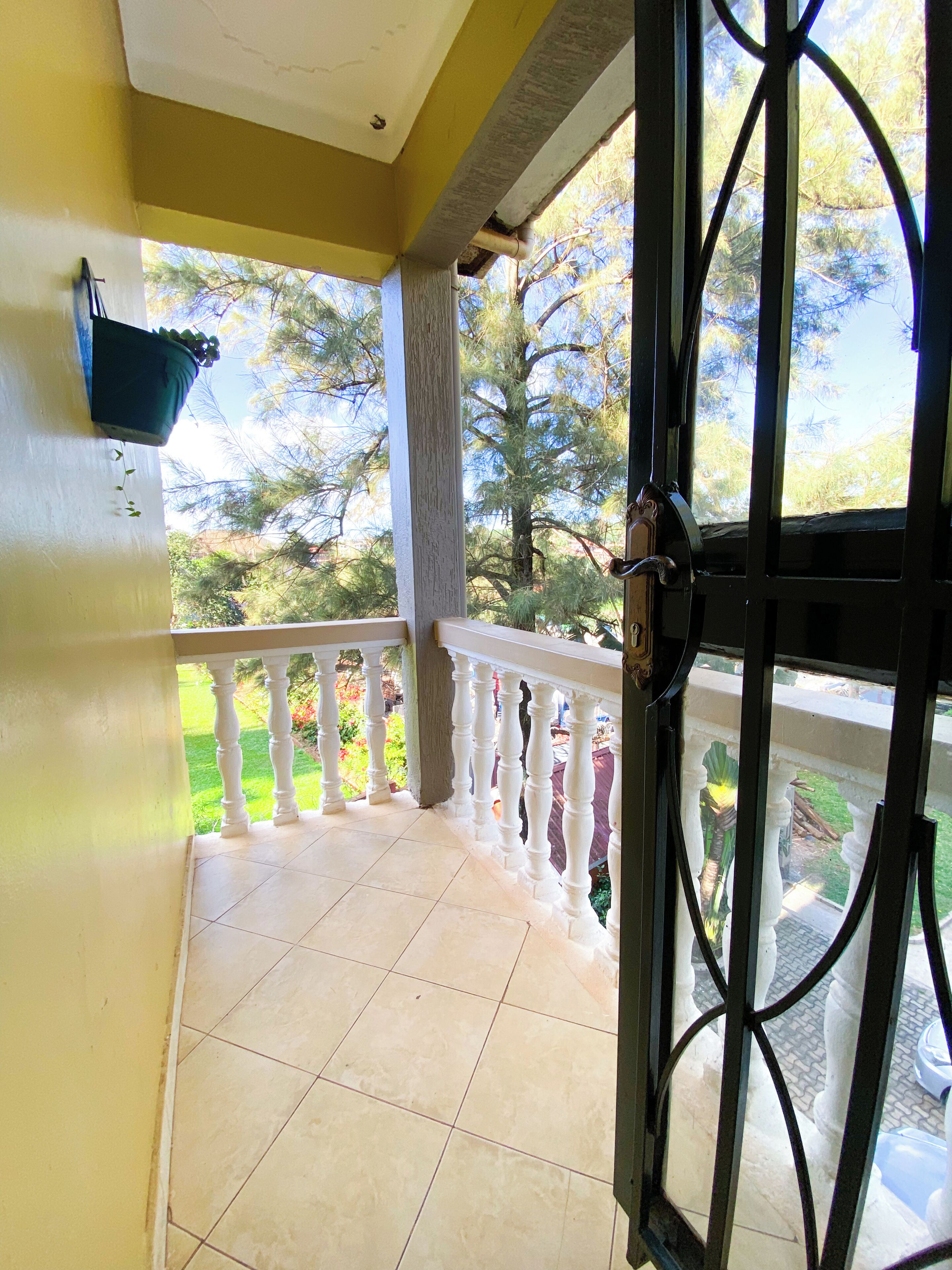 A balcony with a tiled floor, white balustrade, and a view of trees and a garden.