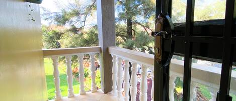 Un balcon doté d’un sol carrelé, d’une balustrade blanche et offrant une vue sur des arbres et un jardin.