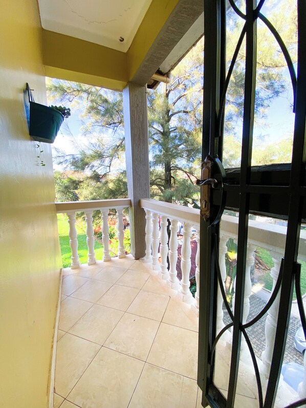 A balcony with a tiled floor, white balustrade, and a view of trees and a garden.