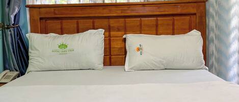 Una cama con dos almohadas, un cabecero de madera y una ventana con cortinas estampadas.