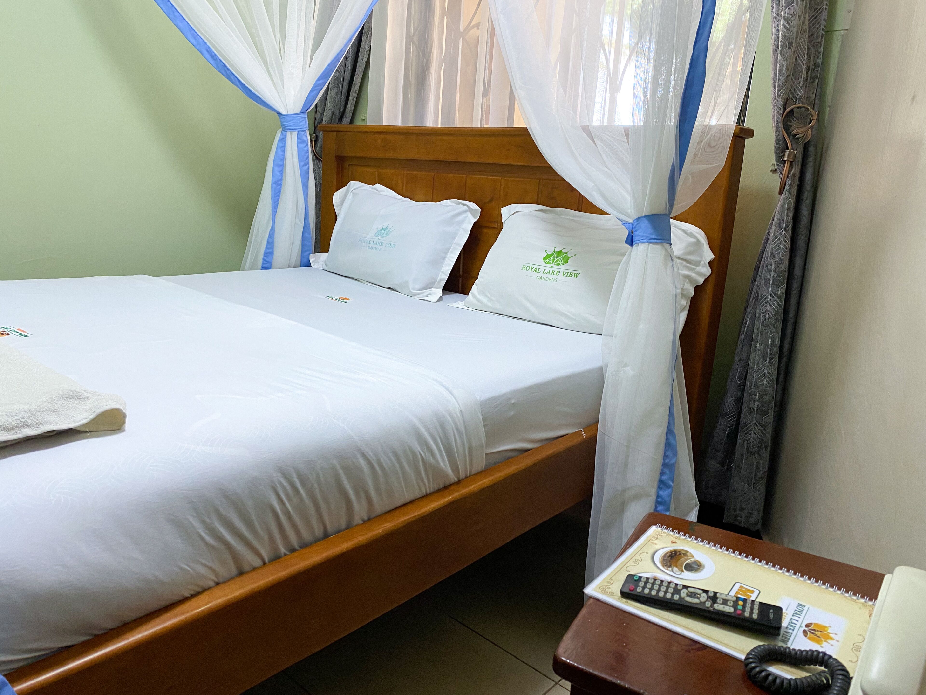 A bed with a canopy, a bedside table with a remote control, and a pillow with a logo.