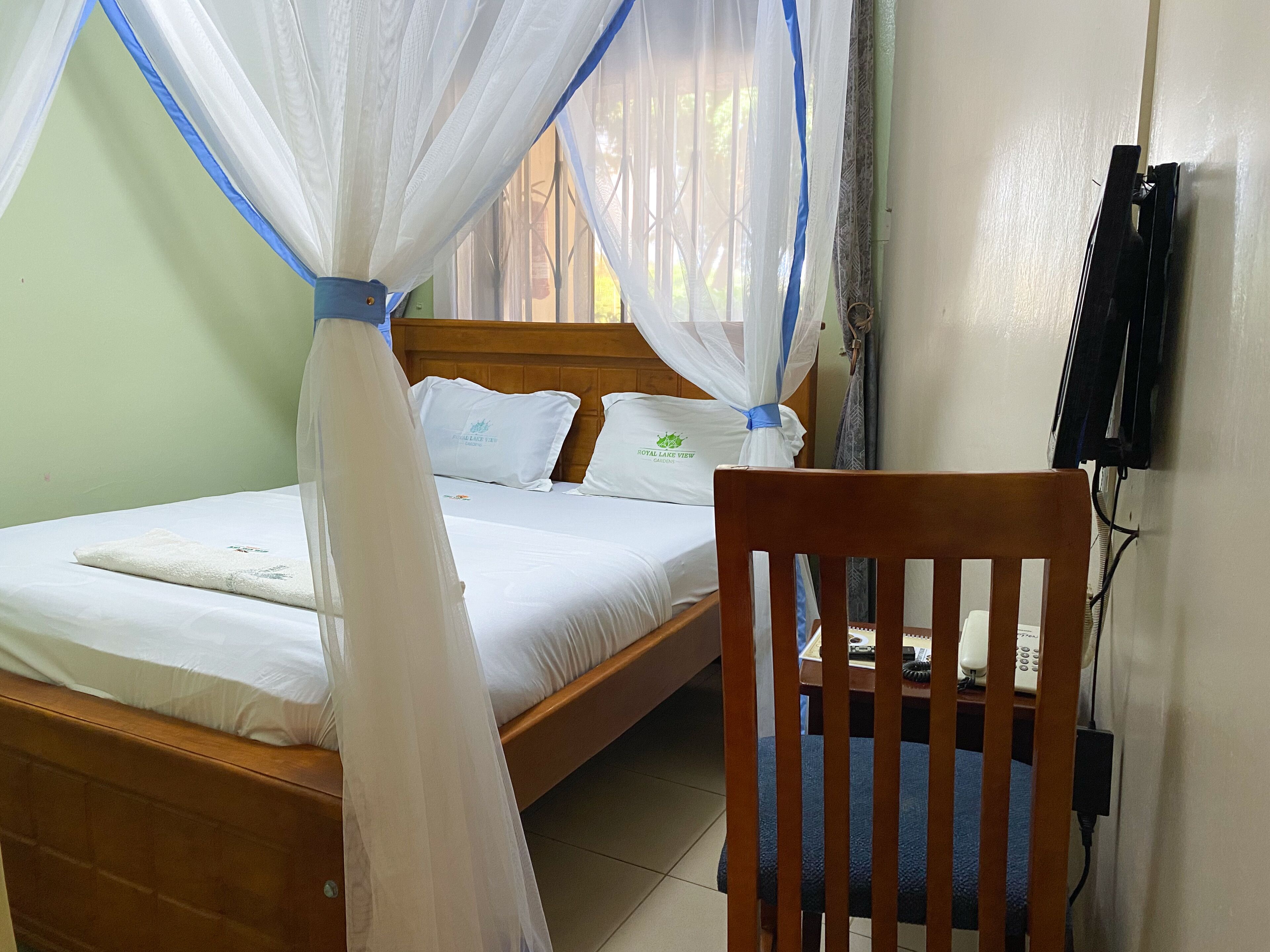 A bedroom with a bed, a wooden chair, a bedside table, and a TV mounted on the wall.