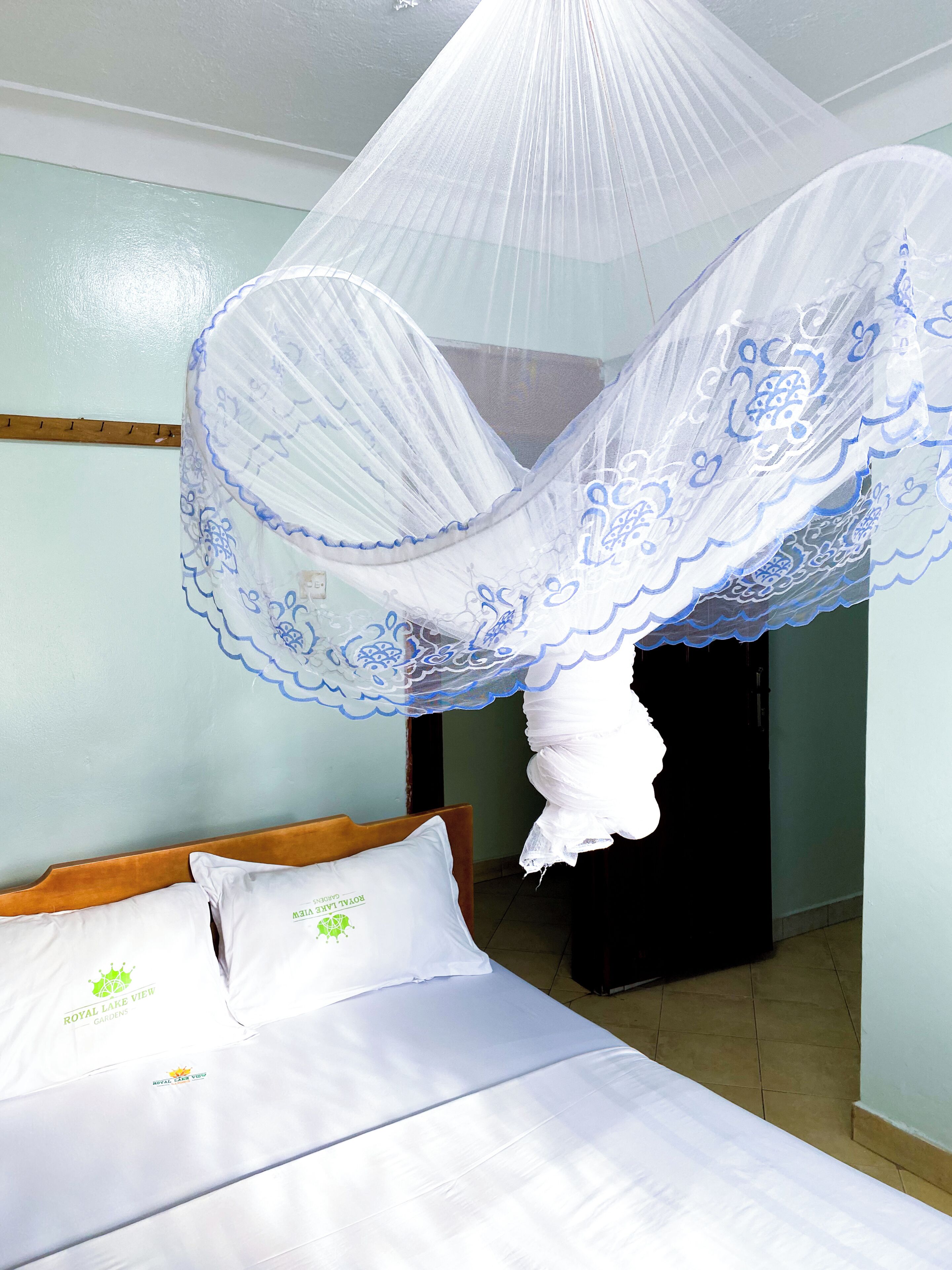 A bed with white bedding and pillows, a wooden headboard, and a mosquito net with blue trim.