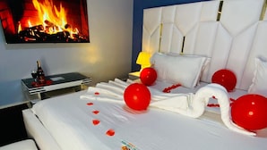 A hotel room with a bed, a flat-screen TV, a wall-mounted fan, and a fireplace. - Royal Lake View Gardens (Kampala)