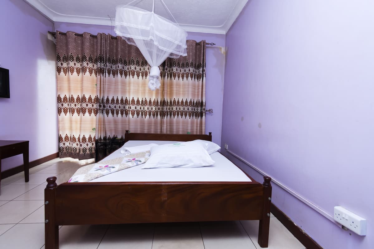 A bedroom with a wooden bed, a mosquito net, patterned curtains, and a white wall socket.