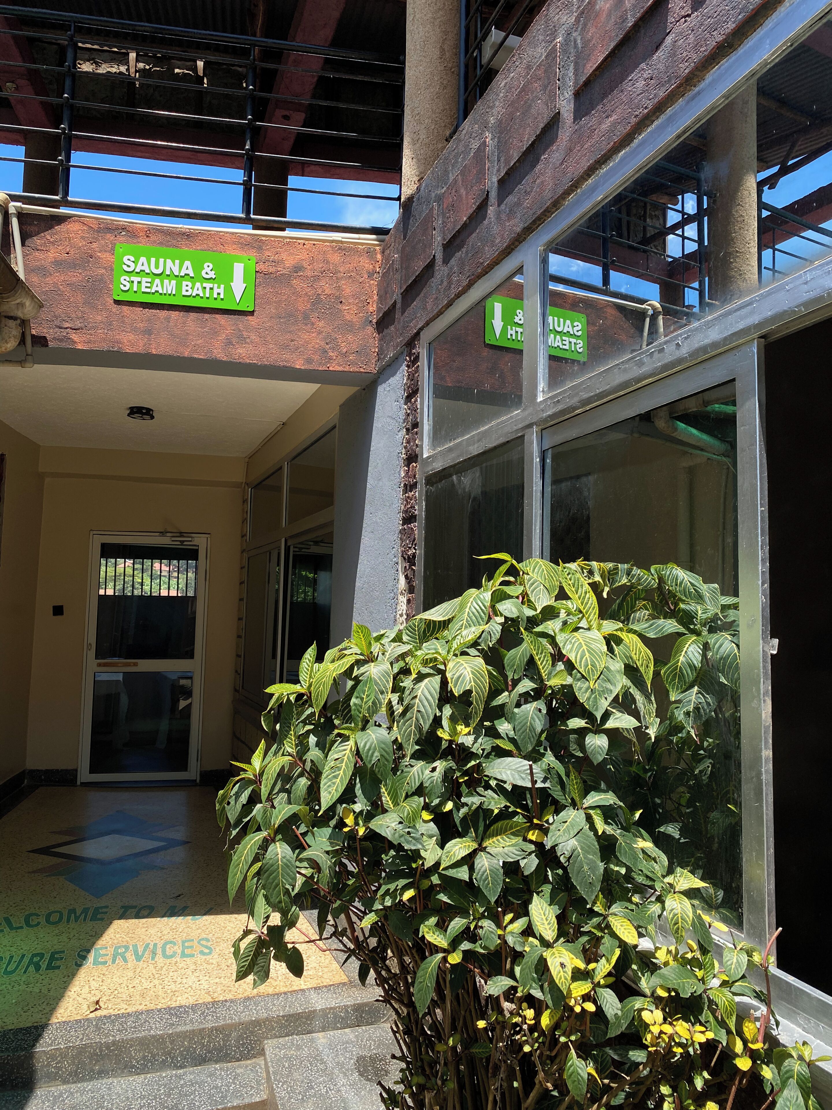 A building entrance with a sign for a sauna and steam bath, a staircase leading to a second floor, and a welcome sign for pure services.