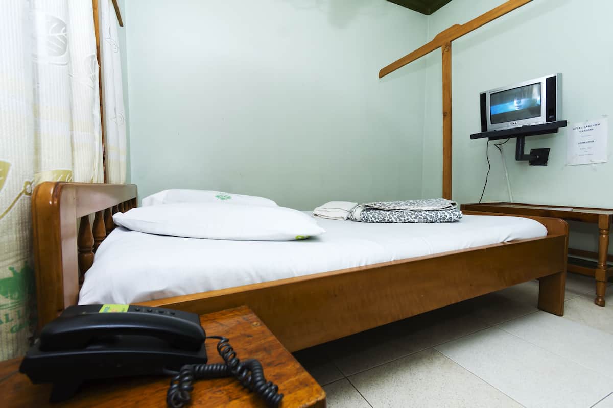 A single bed with a wooden frame, a bedside table with a telephone, and a television mounted on the wall.